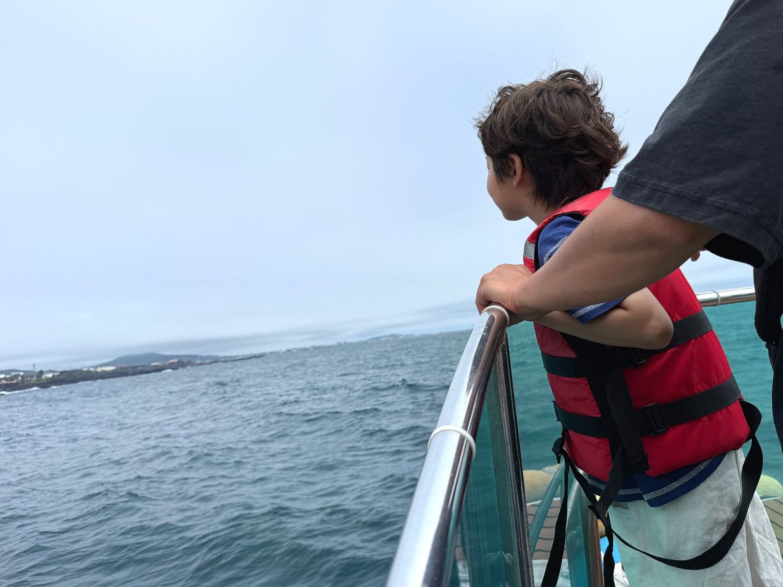 구명조끼를 착용한 아이와 보호자가 출항 전 제주 바다를 바라보는 모습